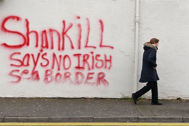 A woman walks past freshly painted loyalist graffiti in the Shankill area of Belfast on January 31. The graffiti says 'Shankill says no Irish sea border'.