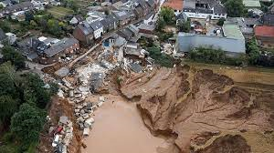 Extreme flooding that occurred in Germany and Belgium in 2021 caused by extreme weather. In this example of a built-up area with rows of houses and large buildings, the flooding has caused extensive damage to property as one side of a street and the housing properties that were present there has now been completely consumed by flooding. Rubble and debris is evident in the water and muddy banks.