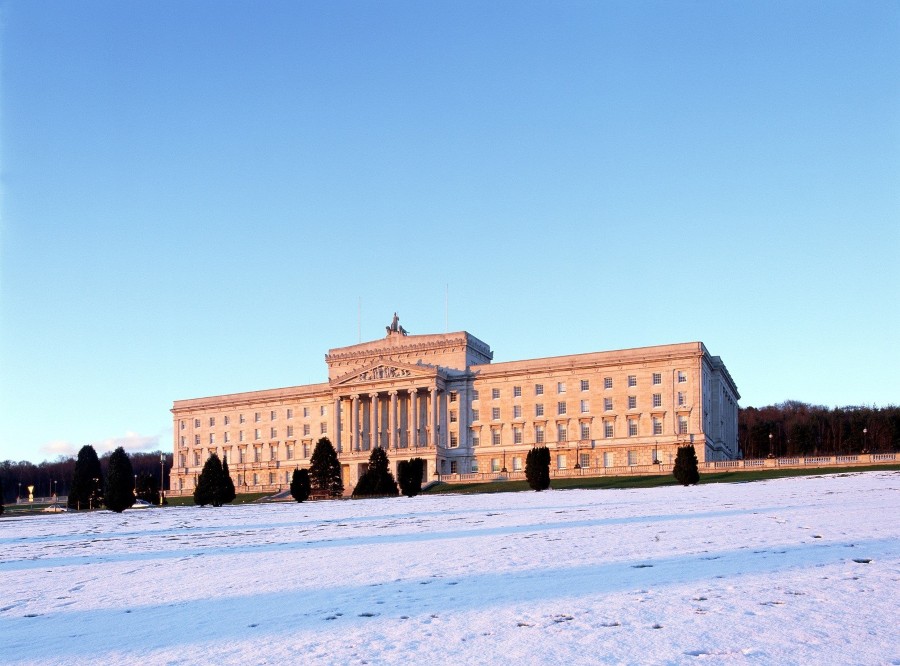 Parliament Buildings seen from the outside in winter. There is snow covering the front lawn and a blue sky