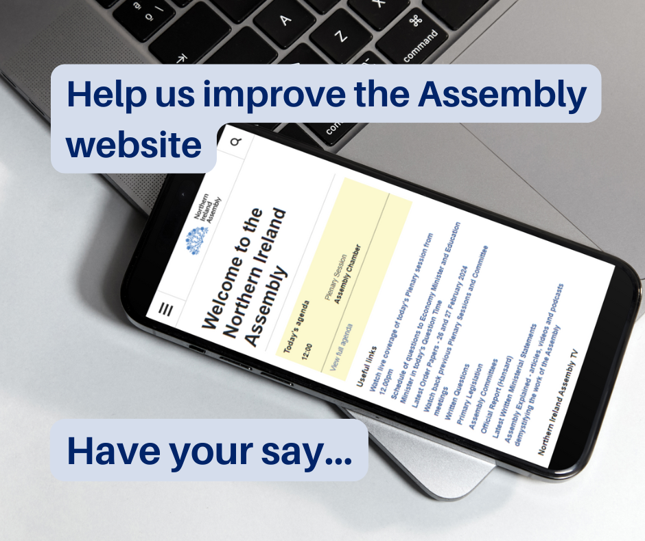 A mobile phone sits on top of a laptop keyboard. The mobile phone is displaying the homepage of the Northern Ireland Assembly website. Text in the image reads: 'Help us improve the Assembly website - have your say...'