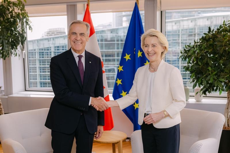 image shows the President of the European Commission, Ursula von der Leyen on the right shaking hands with the Prime Minister of Canada of Canada, Mark Carney on the left. The Canadian and European Union flags are behind them.