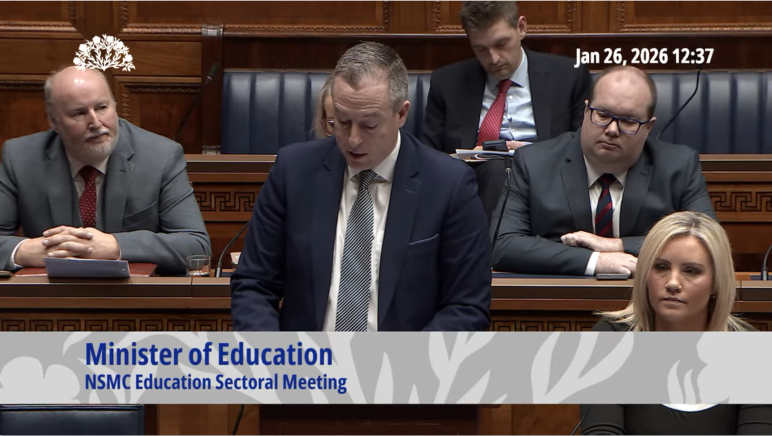 image shows the Education Minister giving a speech in the Assembly Chamber. 