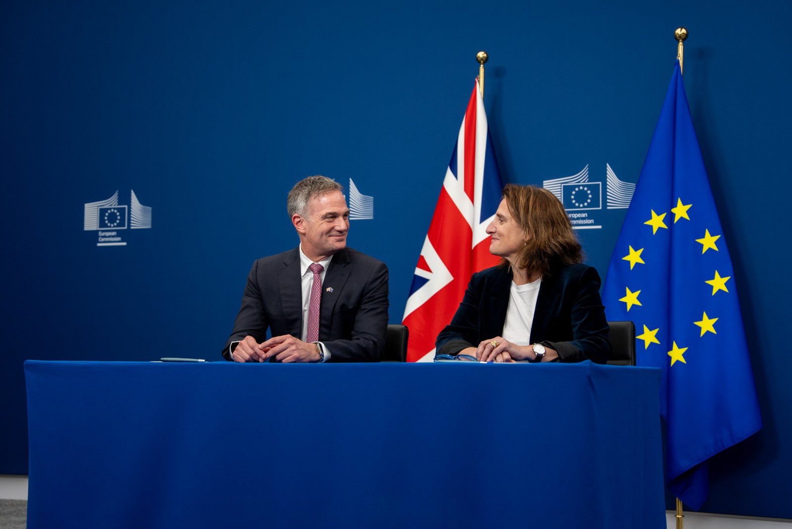 image shows the Secretary of State for Business and Trade, the Rt Hon Peter Kyle MP on the left andTeresa Ribera, Executive Vice-President of the European Commission for Clean, Just and Competitive Transition on the right. They are seated behind a small table with a blue covering. There is a Union Jack and EU flag in the background 