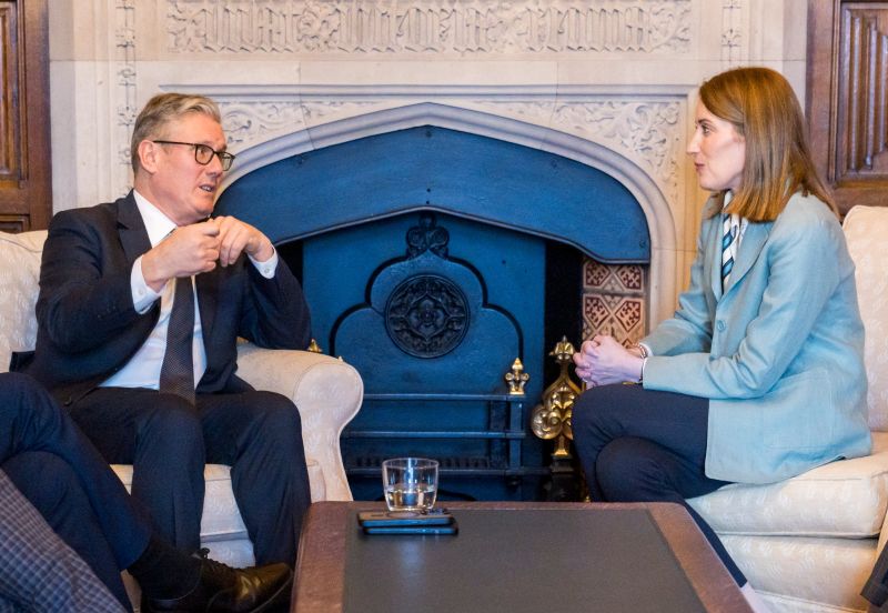image shows the Prime Minister Sir Keir Starmer MP seated on the left andhe President of the European Parliament, Roberta Metsola seated on the right. There is a small coffee table between them and an ornate fireplace in the background. They are looking towards each other and talking. 